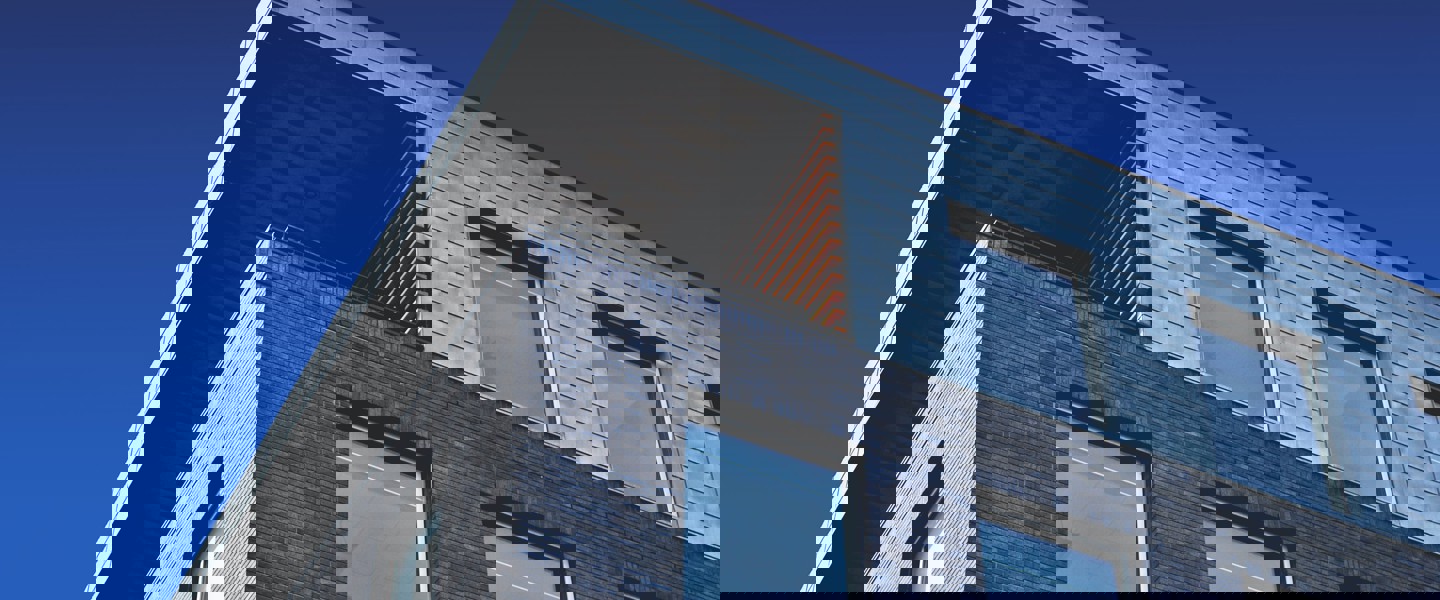 Modern gebouw met een metalen dak en een bakstenen gevel, tegen een achtergrond van een blauwe lucht.