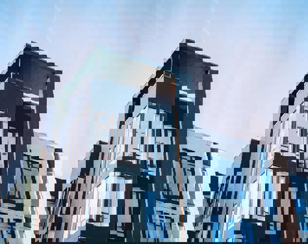 Moderne appartementencomplex met grote ramen en een strakke, donkergekleurde gevel, tegen een heldere blauwe lucht.