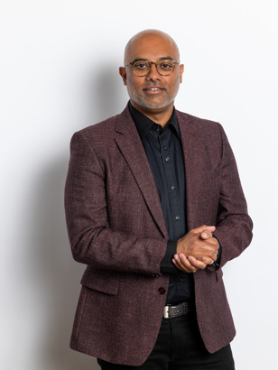 Amer in een bordeauxkleurig blazer met samengevoegde handen, staand voor een witte achtergrond.