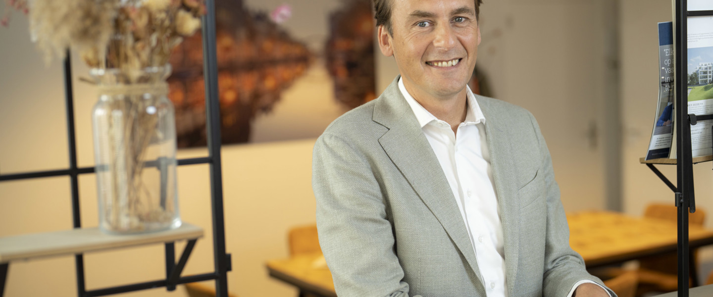 Daniel Van Egmond Credion in een lichtgrijze blazer staat voor een bureau in een moderne kantooromgeving met planten en een kunstwerk op de achtergrond.