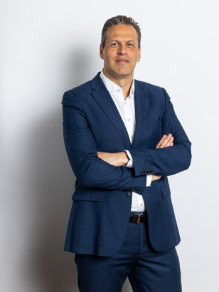 Coen Vreeswijk in een formele donkere blazer met gekruiste armen op een neutrale achtergrond.