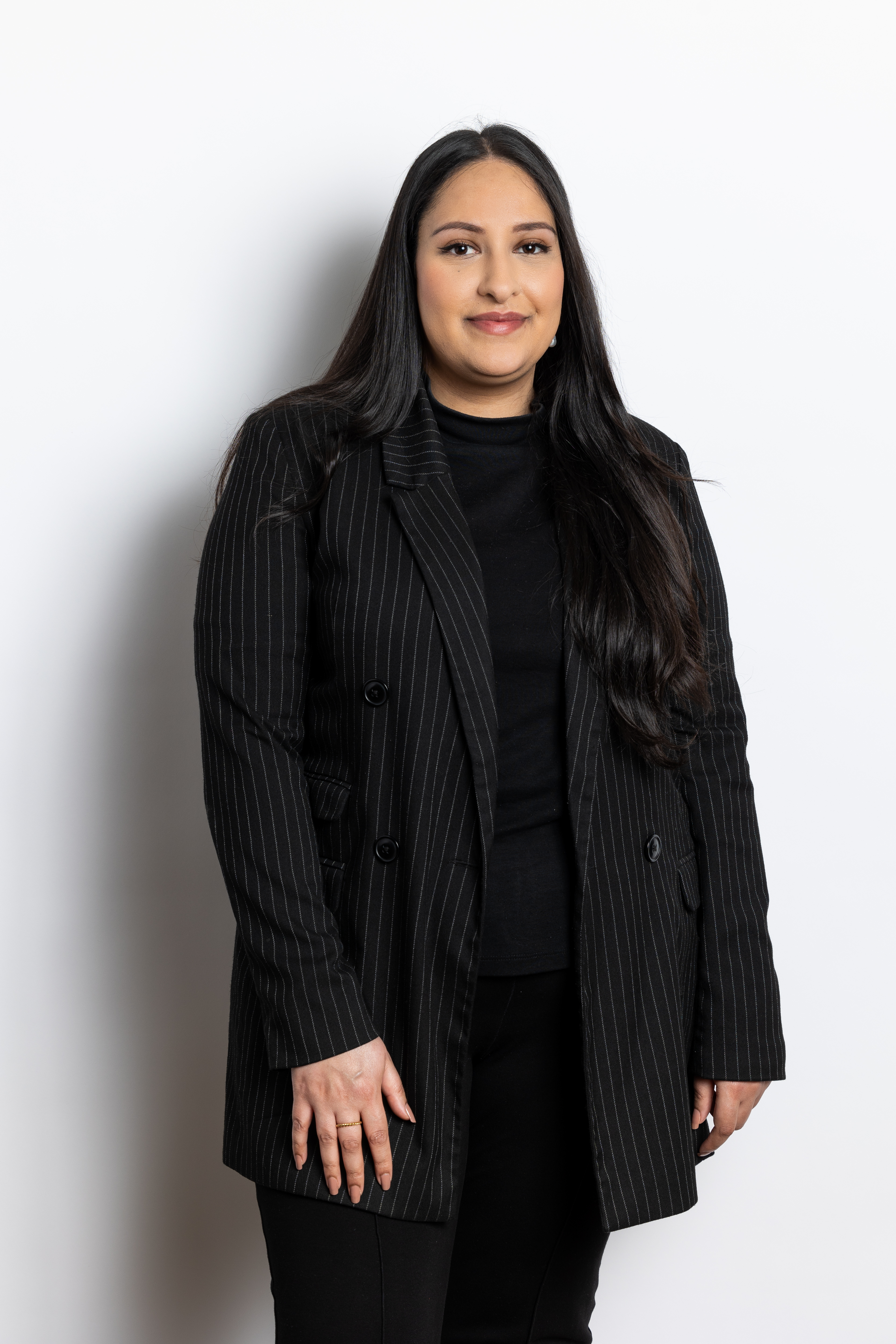 Anju Chouhan in een zwart-witte gestreepte jas staat rechtop met lang, glanzend haar en een neutrale gezichtsuitdrukking.