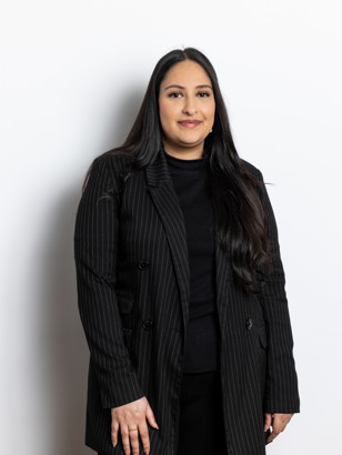 Anju Chouhan in een zwart-witte gestreepte jas staat rechtop met lang, glanzend haar en een neutrale gezichtsuitdrukking.